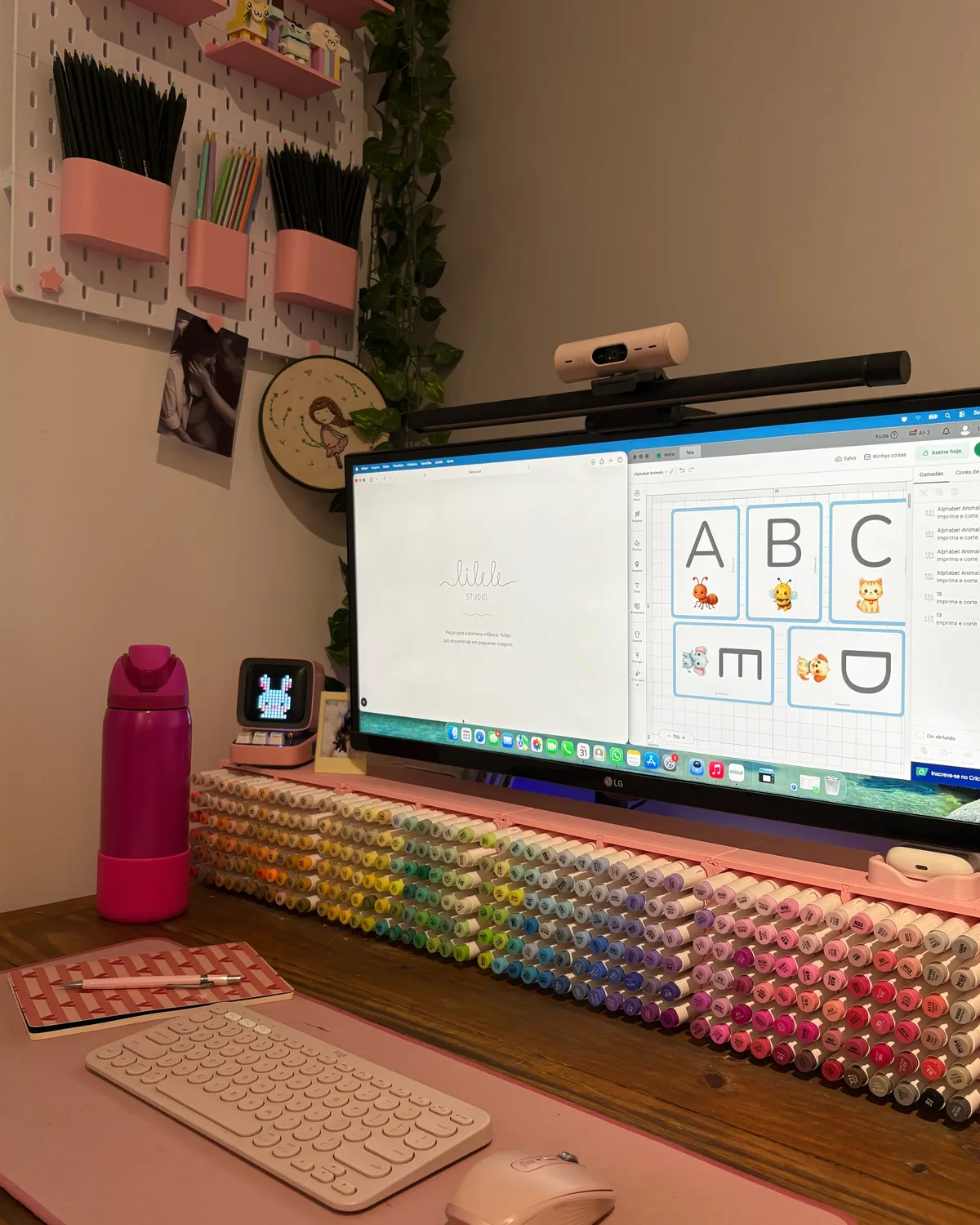Bancada do ateliê com cartas em criação no monitor e materiais de desenho organizados à mão